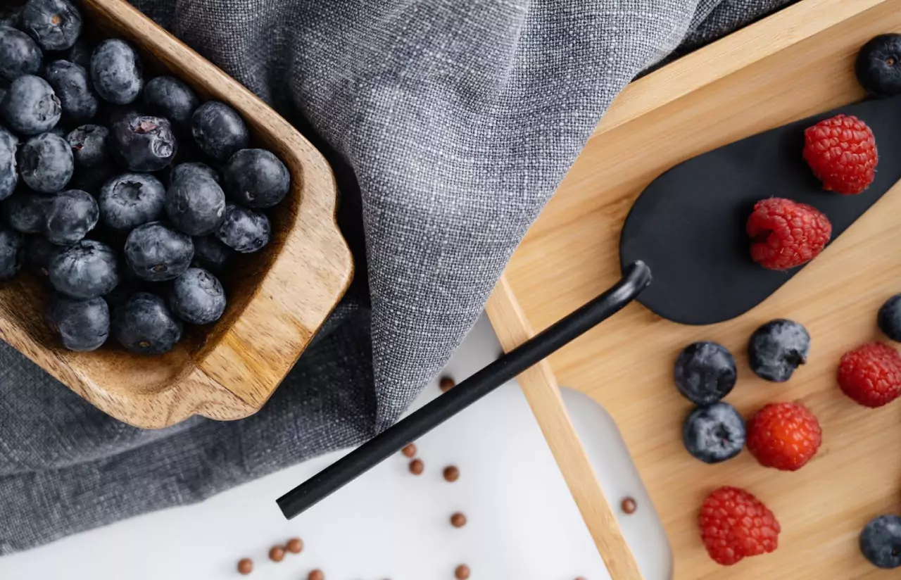 blueberries in a wooden dish, next to a wooden board with raspberries and blueberries