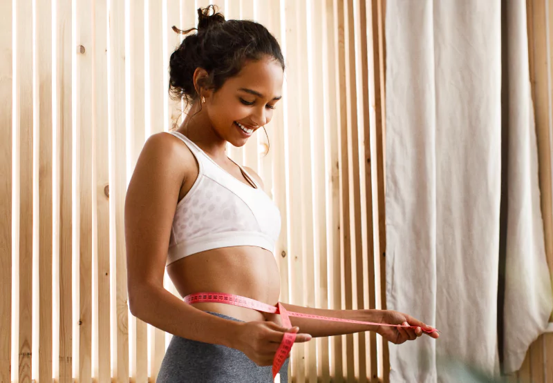 a girl in workout clothes measuring her waist