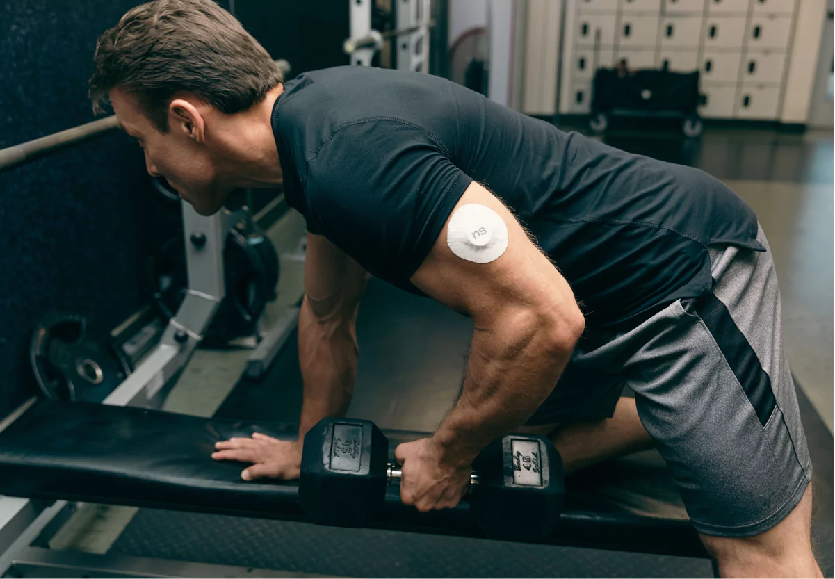 a man with a nutrisense cgm patch doing a dumbbell row