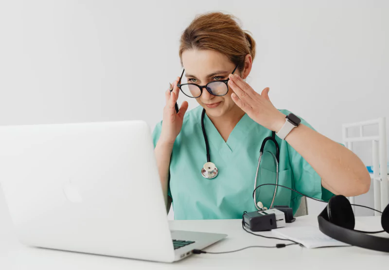 a doctor touching her glasses while looking at her computer