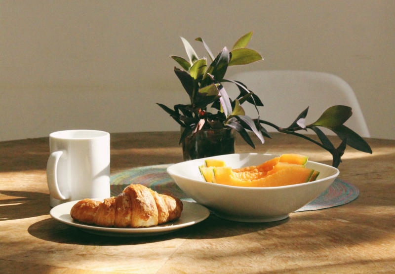 Dining table with coffee, papaya, and a croissant
