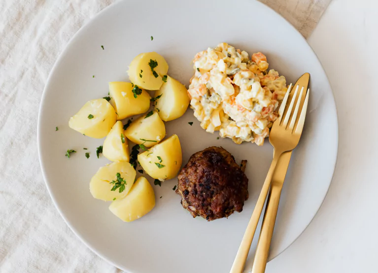 a plate with potatoes, meat and salad with cutlery